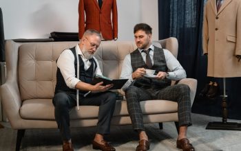 Two men discussing custom suit fitting in an elegant tailoring atelier with sophisticated decor.